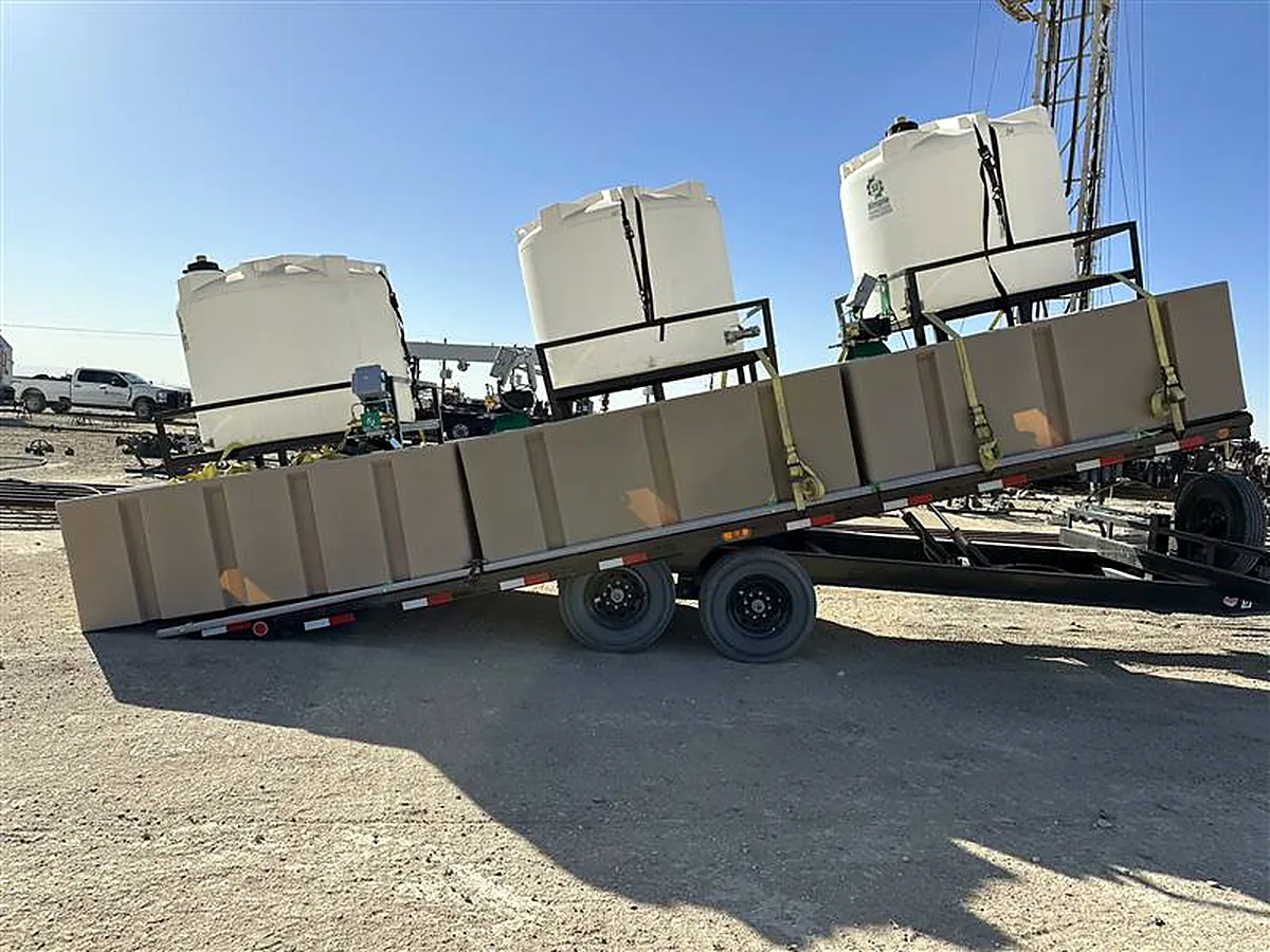 Chemical injection skids on a tilted trailer being unloaded at a wellsite